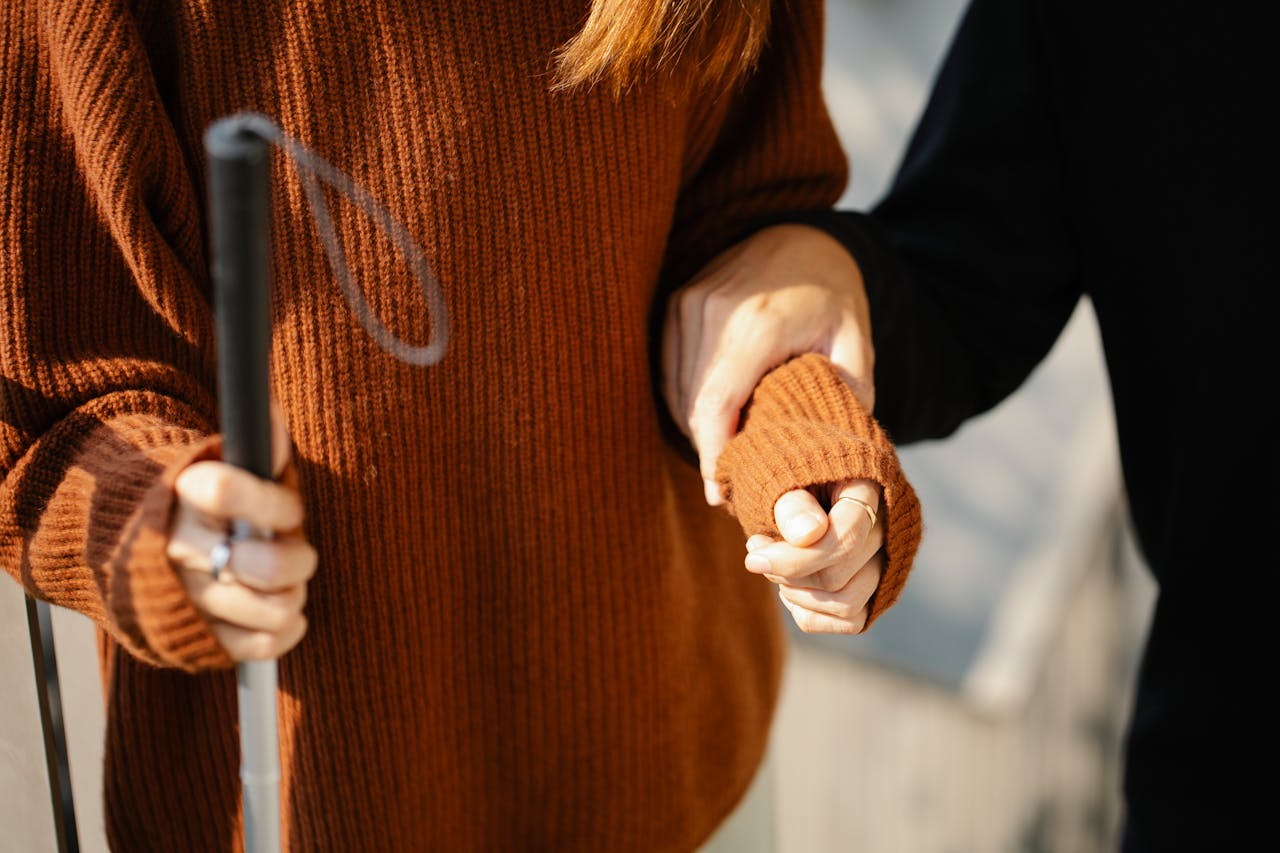 Close-up of two people holding hands, one with a walking cane symbolizing support and visual aid.