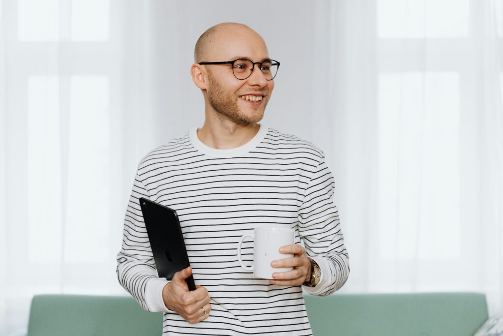 Happy bald man with eyeglasses holding a digital tablet and mug, smiling indoors.
