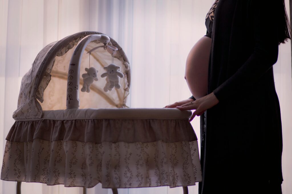 Silhouette of a pregnant woman next to a baby cradle in a softly lit room.