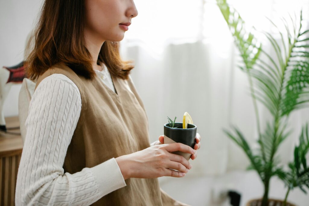 Close-up of a woman holding a herbal tea cup indoors with natural light and plant decor.