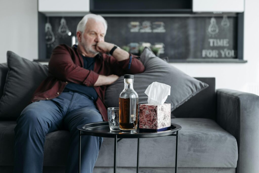 A senior man sits pensively with a bottle of whiskey, evoking a somber mood.