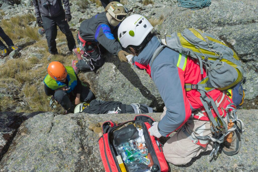 A mountain rescue team helps an injured climber with medical equipment in rocky terrain.