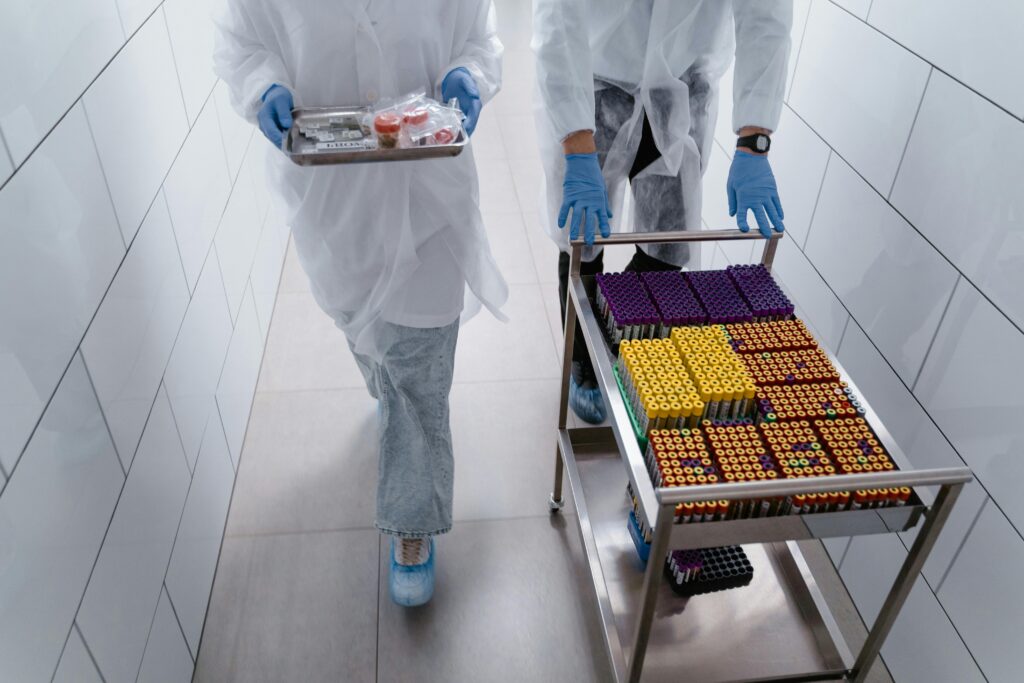 Lab workers in protective gear moving sample trays in a sterile laboratory hallway.